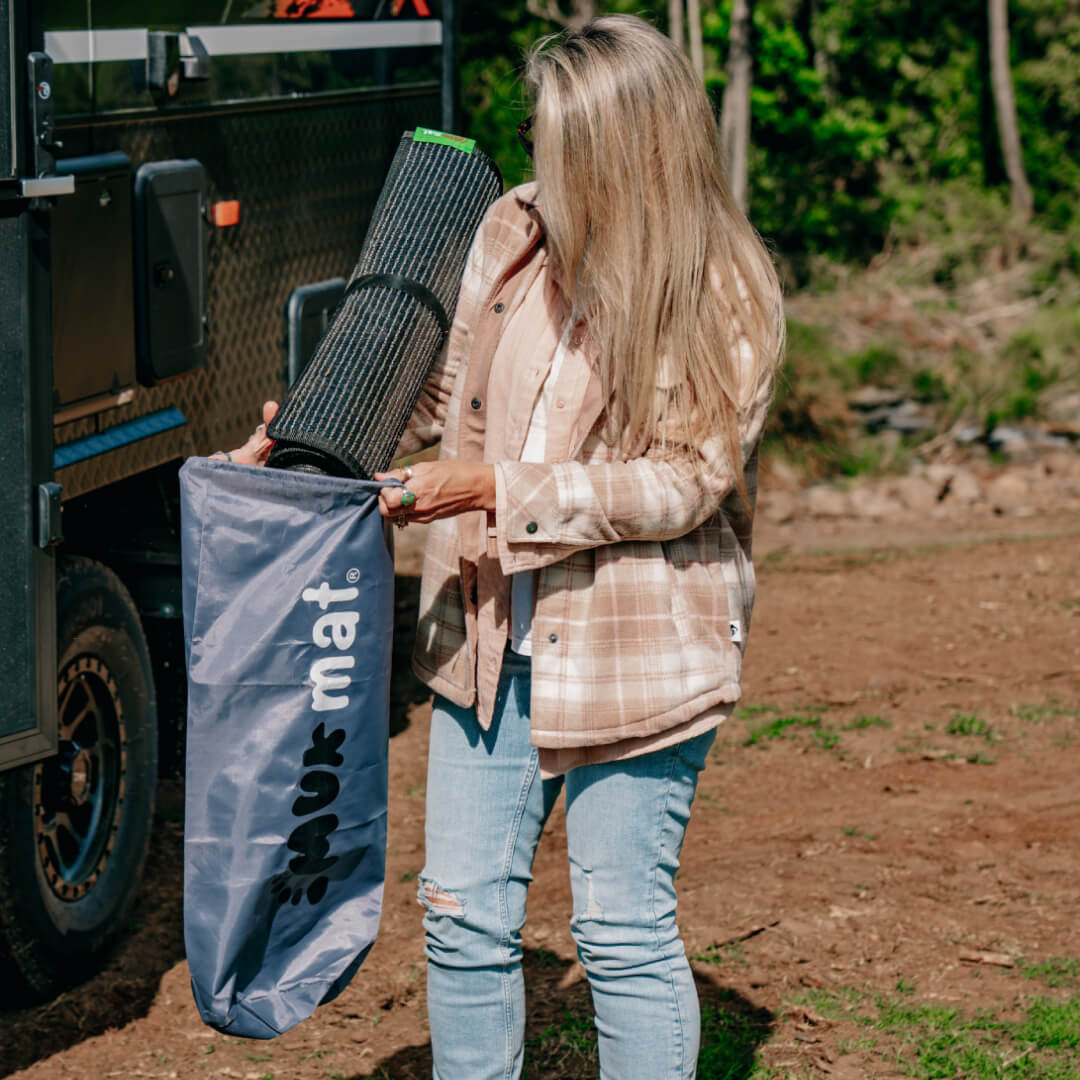 woman packing muk mat caravan ground mat into storage bag at campsite
